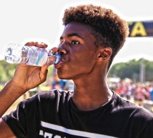 A young man drinking bottled water outdoors at a sporting event, showcasing hydration and fitness.