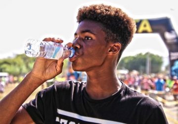 A young man drinking bottled water outdoors at a sporting event, showcasing hydration and fitness.