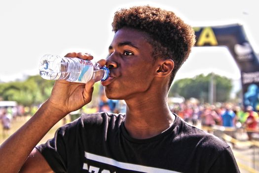 A young man drinking bottled water outdoors at a sporting event, showcasing hydration and fitness.